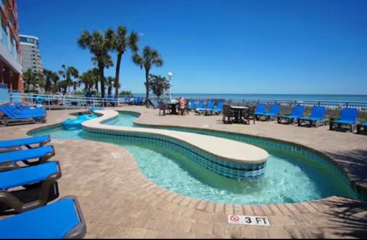 Lazy river pool with blue loungers and ocean backdrop